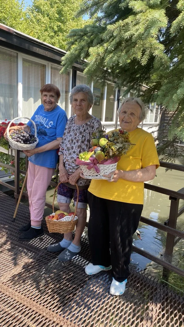 Три мешканки на веранді зі святковими кошиками з яблуками, виноградом і квітами.